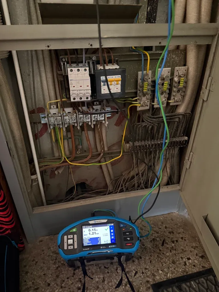 Měření impedance poruchové smyčky přístrojem Metrel Eurotest při revizi elektroměrového rozvaděče bytového domu — nové jističe OEZ a proudový chránič Eaton vedle původních svorkovnic